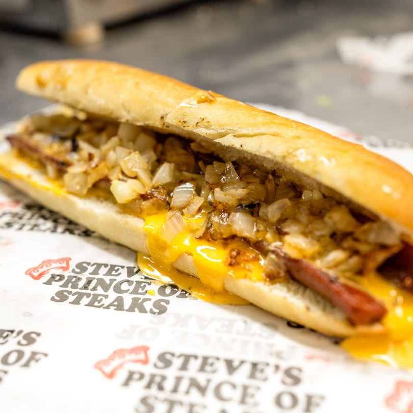 Steve's Prince of Steaks cheesesteak with melted cheese and grilled onions on branded paper.